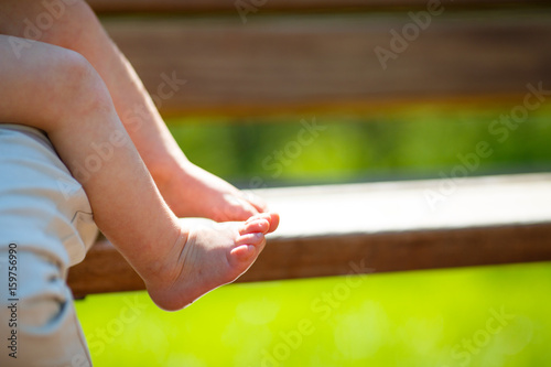 barefooted kid with covered gooseflesh sits on his mother's lap on a wooden bench in the rays of the spring sun