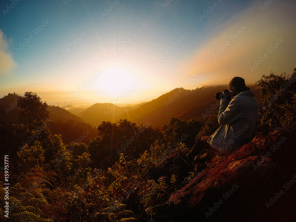 Alone man on the top of the mountains. He shooting cloudy sky and colorful sunrise.