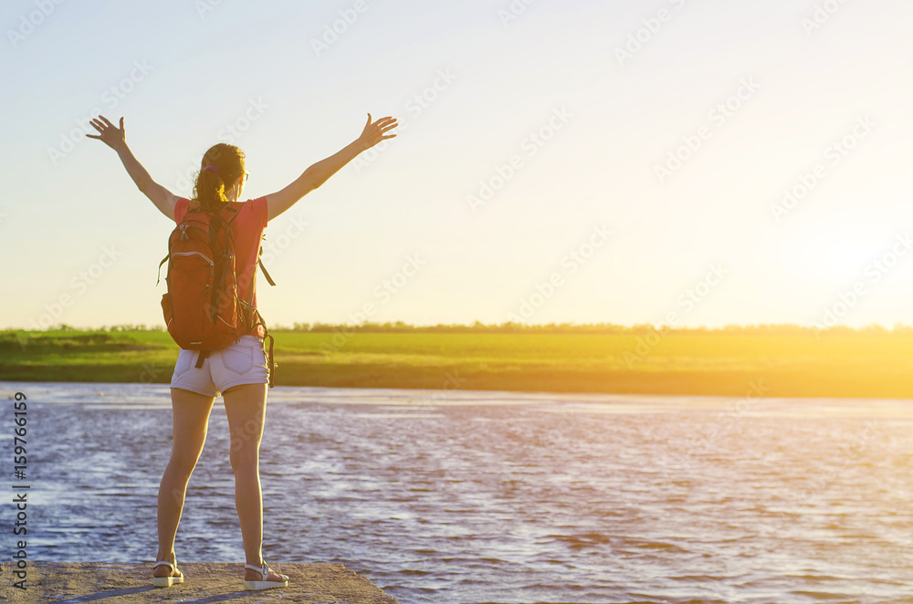 Naklejka premium A happy woman is standing on the pier and enjoying the sunset, free space.
