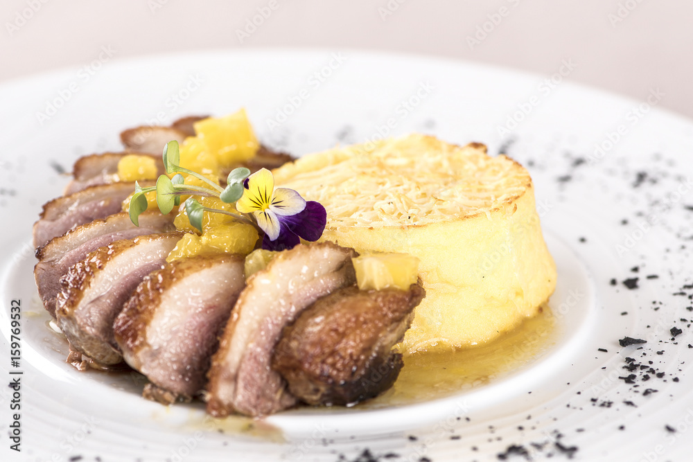 Luxurious dish with slices of duck breast, pineapple pieces, sweet sauce, with potato puree and parmesan, decorated with eatable flowers and red and green leafs, placed on white plate, light backgroun Luxurious dish with slices of duck breast, pineapple pieces, sweet sauce, with potato puree and parmesan, decorated with eatable flowers and red and green leafs, placed on white plate, light backgroun