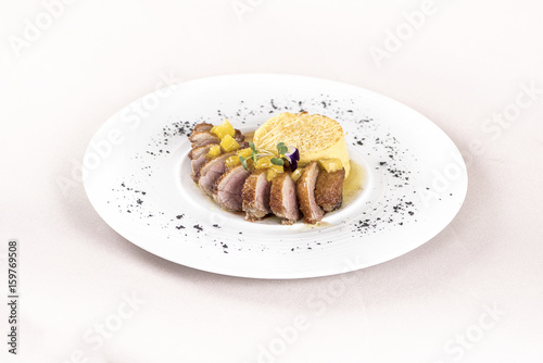 Luxurious dish with slices of duck breast, pineapple pieces, sweet sauce, with potato puree and parmesan, decorated with eatable flowers and red and green leafs, placed on white plate, light backgroun