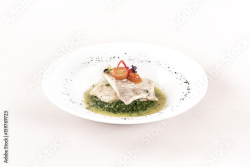Perch fillet with spinach, sauce and tomato, decorated with eatable flowers and red leafs, placed on white plate, light background, isolated