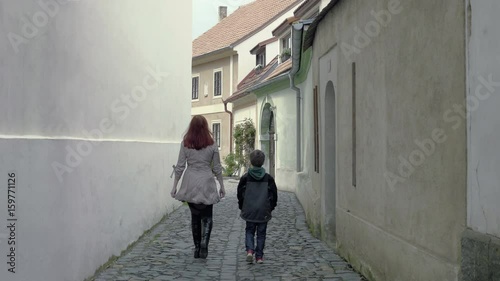 Mother and her son leave the camera in a narrow medieval aisle. A red-haired woman with a little boy is going to meet the sun. Positive, promising atmosphere. Static day stabilized shot.