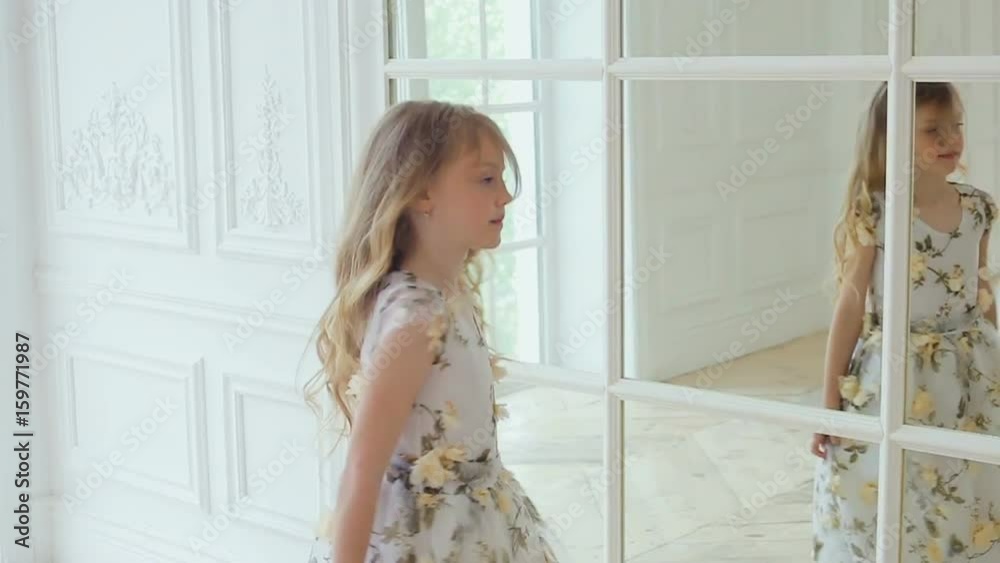 girl in long dress with flowers turns dancing in front of a large mirror