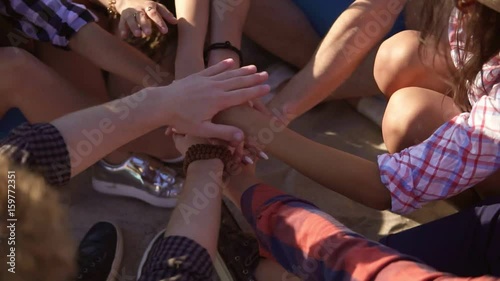 Closeup view of many hands united together and raised up. Teamwork and friendship concept. Group of friends sitting on easychairs on the beach on a summer evening. Slowmotion shot