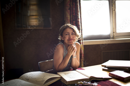 portrait of female smiling at camera while drawing inspration from books