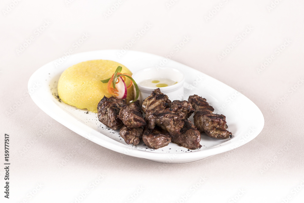Delicious grilled pork, with polenta and garlic sauce, decorated with red and green leafs, placed on white plate, light background, isolated Delicious grilled pork, with polenta and garlic sauce, decorated with red and green leafs, placed on white plate, light background, isolated