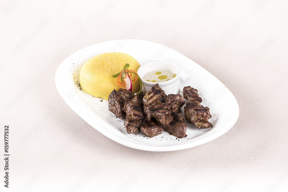 Delicious grilled pork, with polenta and garlic sauce, decorated with red and green leafs, placed on white plate, light background, isolated Delicious grilled pork, with polenta and garlic sauce, decorated with red and green leafs, placed on white plate, light background, isolated