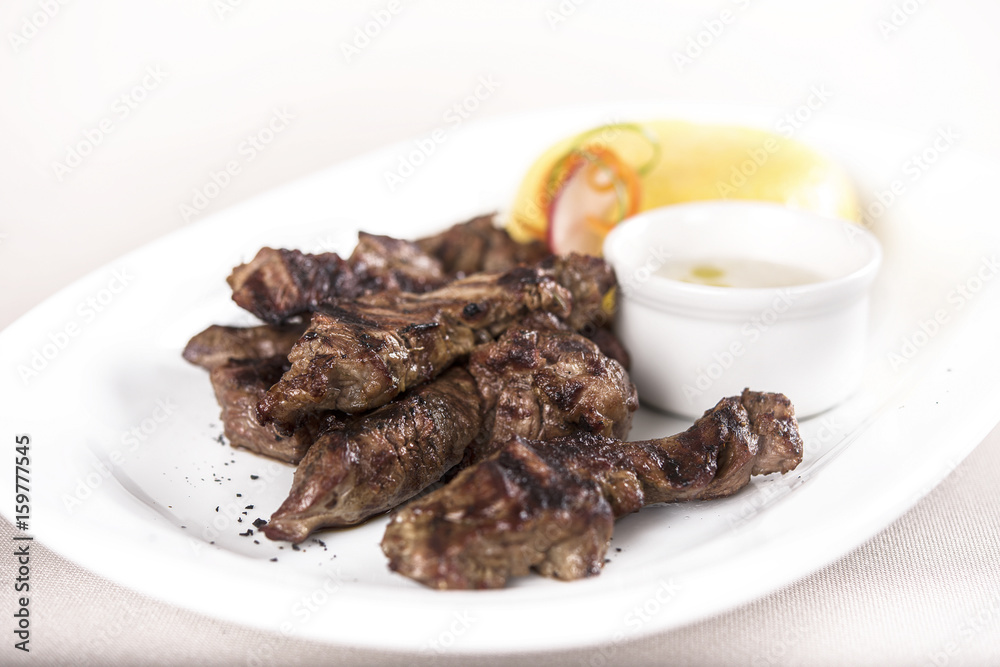 Delicious grilled pork, with polenta and garlic sauce, decorated with red and green leafs, placed on white plate, light background, isolated Delicious grilled pork, with polenta and garlic sauce, decorated with red and green leafs, placed on white plate, light background, isolated