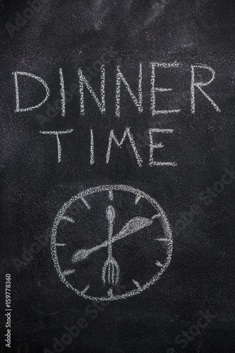 Dinner time text with clock drawn with white chalk on blackboard