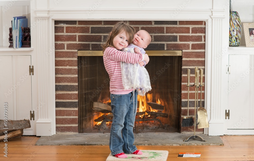 Portrait of a young smiling girl hold a baby doll in front of a fireplace dressed for valentine's day Portrait of a young smiling girl hold a baby doll in front of a fireplace dressed for valentine's day