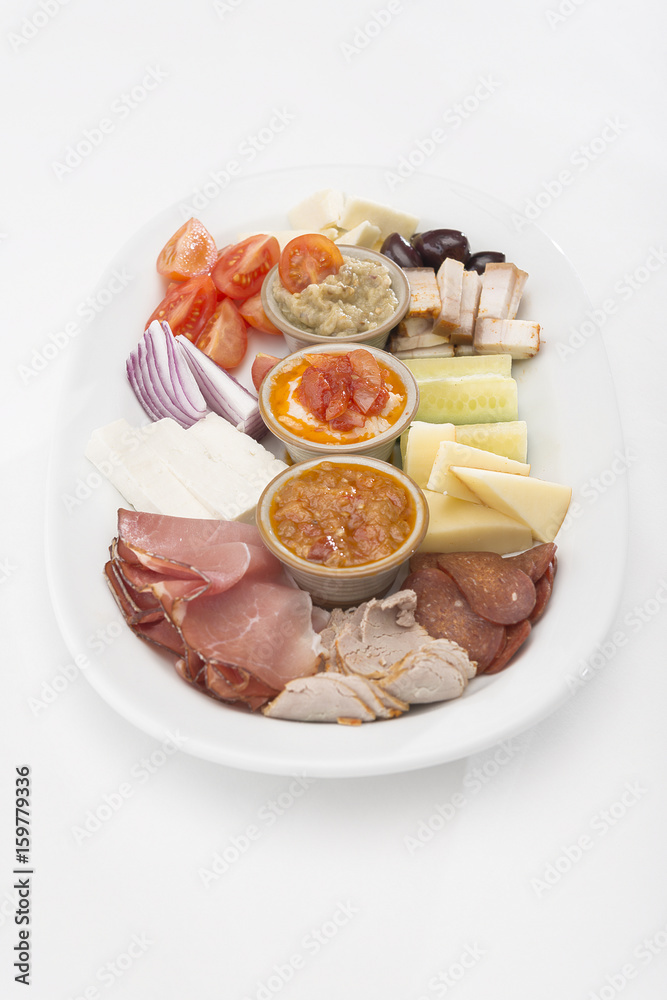 Traditional Romanian food plateau, containing different types of meat and cheese, tomatoes, onion, cucumber, olives and salads: “zacusca”, eggplant salad and beans salad, decorated with herbs, isolate
