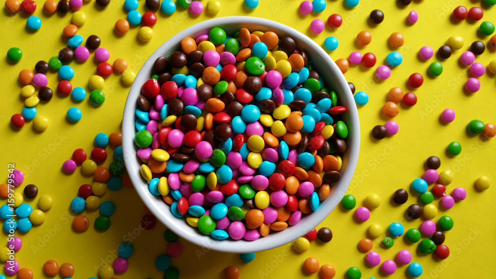 Colorful candy confetti in white pot on yellow background top view