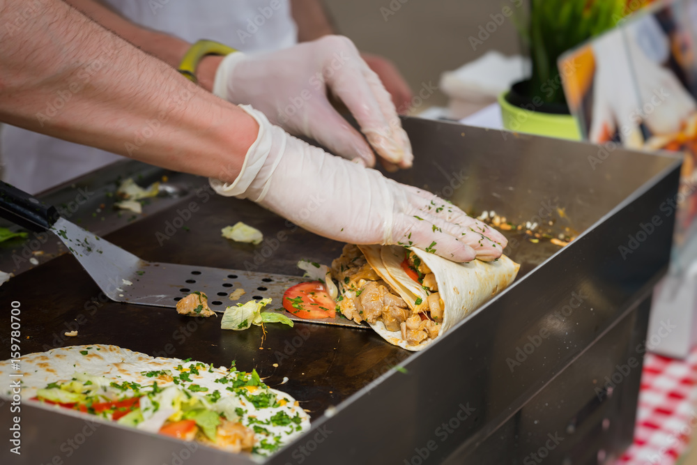 Close-up of hands of cook in gloves preparing fajitas or fajitos. Healthy fresh tortillas with grilled chicken fillet, avocado, fresh salsa. Concept of Mexican food. Party food.