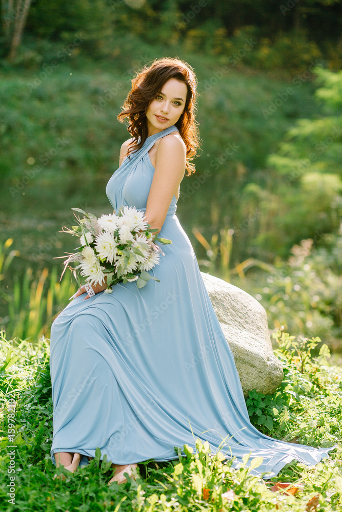 Portraits of a beautiful girl on a sunny day. Bridesmaid. A beautiful woman. Curly hair. Beautiful make-up. Smile on the face and a good mood. Holding a wedding bouquet. Chic hair