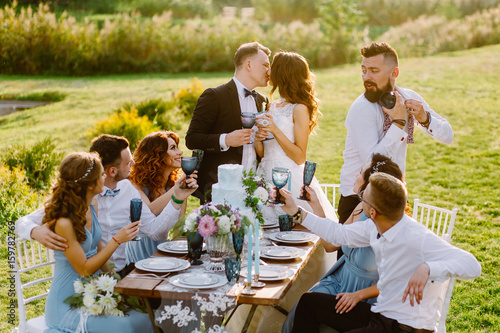 Merry wedding in nature. Guests with the bride and groom are celebrating at the table