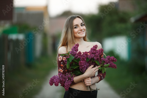 Portrait of a romantic smiling young woman with a bouquet of lilac outdoors shallow depth of field