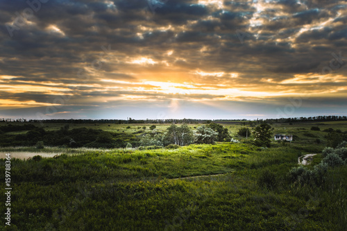 Colorful horizon at sunset on a cloudy summer day amidst colorful clouds of sun rays and a green meadow photo