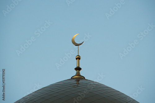 Minaret with a crescent of the Islam mosque at blue sky.