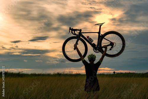 Silhouette of a cyclist with a raised bike in the sun