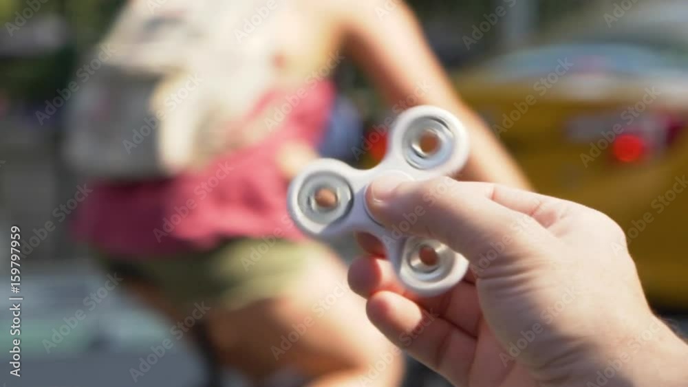 An unidentified male plays with a hand spinner toy in the downtown area of a large city. Slow Motion, shot at 180fps. An unidentified male plays with a hand spinner toy in the downtown area of a large city. Slow Motion, shot at 180fps.