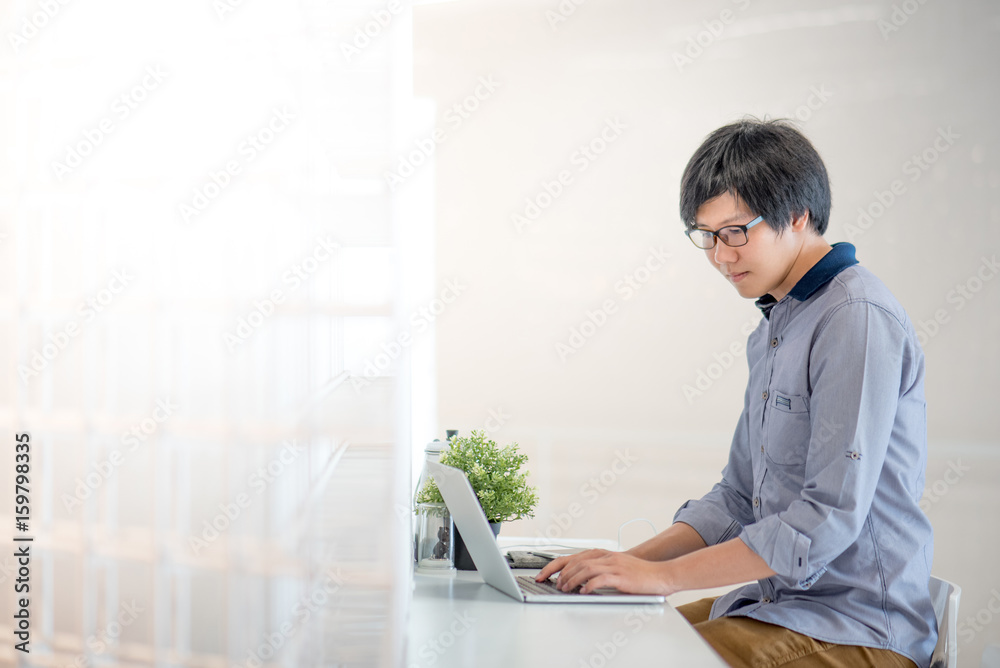 Young Asian man dressed in casual style working in cafe with his laptop computer. Digital nomad and IT modern lifestyle, Co working space for freelance jobs