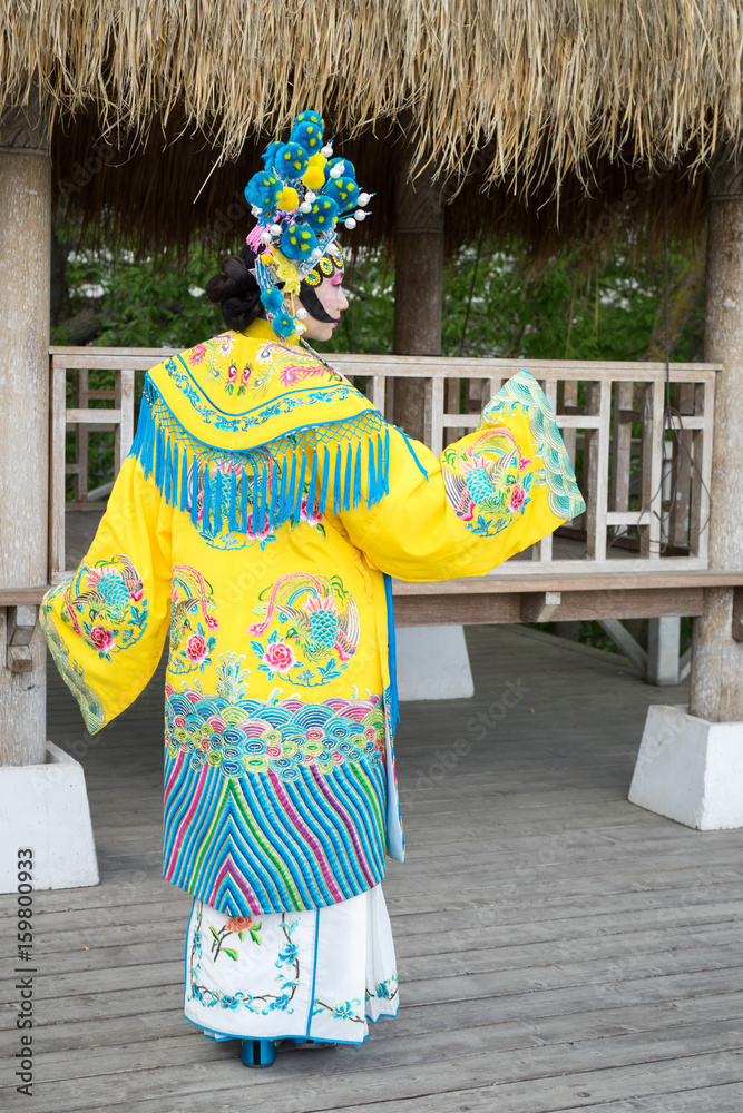 Fototapeta premium beautiful chinese girl in traditional chinese dress with long sleeves and hat with pompons standing back outdoor and turning hand into prifile