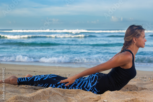 Young woman practicing yoga on the beach at sunrise photo