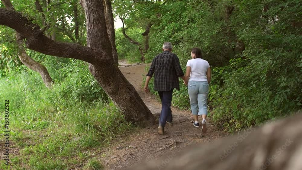 Cheerful middle-aged couple walking in forest Park, man funny jumps to the side. Cheerful middle-aged couple walking in forest Park, man funny jumps to the side.