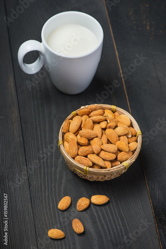 Almond milk in glass with almonds on black wooden table