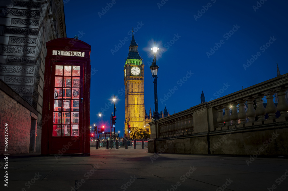 Fototapeta premium Traditional red phone booth or telephone box with the Big Ben in the background, possible the most famous English landmark, at night in London, England, UK