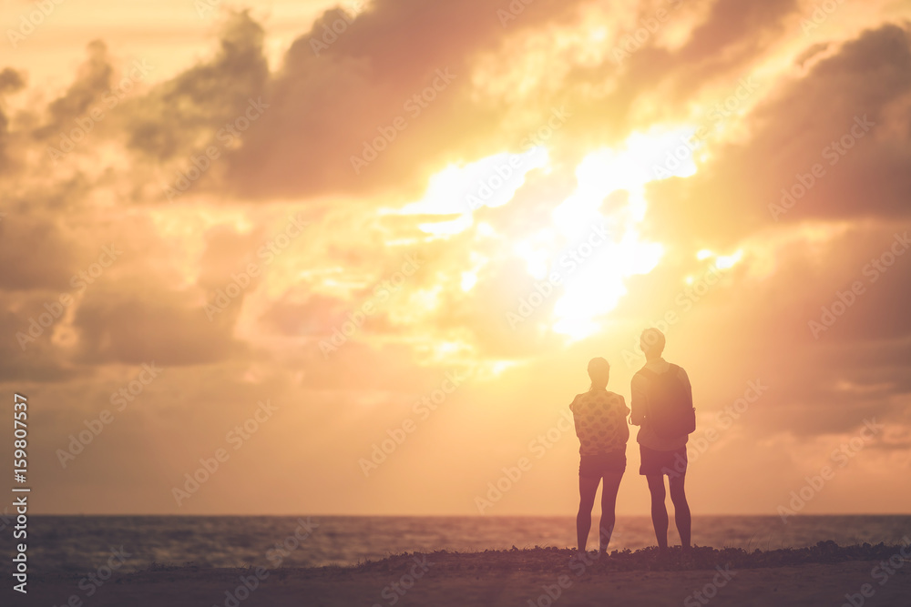 Silhouette of couple people or tourist standing on the beach in sunset time. Warm tone and vintage filter effect