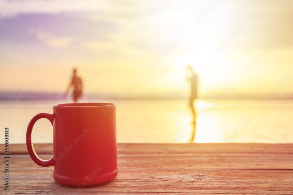 Red coffee cup on wood table at sunset or sunrise beach Red coffee cup on wood table at sunset or sunrise beach