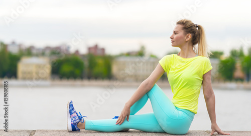 Billede på lærred Young sporty woman in bright clothes sitting on the narrow railings