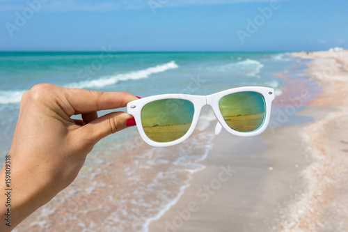 Sunglasses in hand on background of the beach
