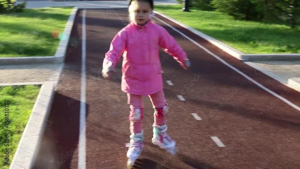 A seven-year-old girl learns rollerblading in a summer park on a bicycle path