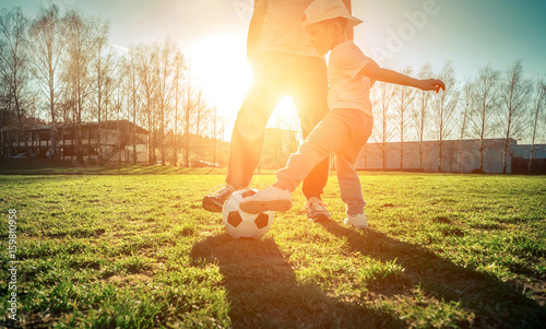 Father and son playing together with ball in football under sun