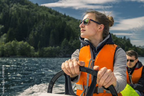 Fotografi Portrait of young and attractive woman close up driving the motorboat, Norway