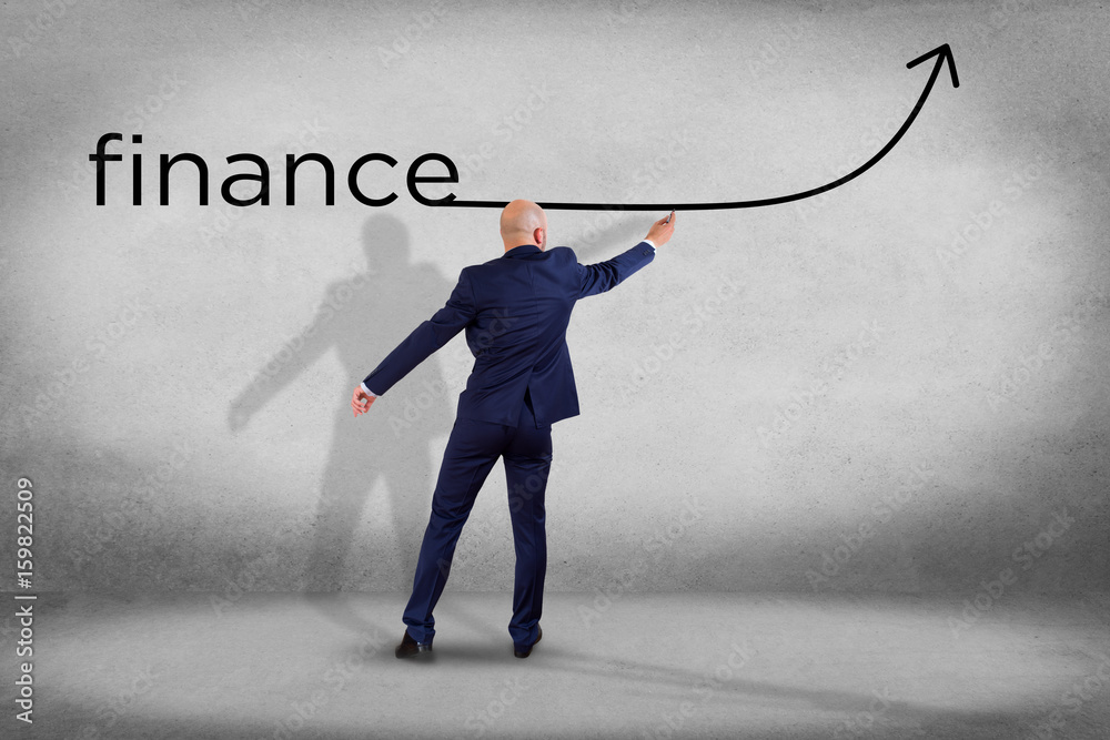 Businessman in front of a wall writing the word finance with a arrow - business concept Businessman in front of a wall writing the word finance with a arrow - business concept