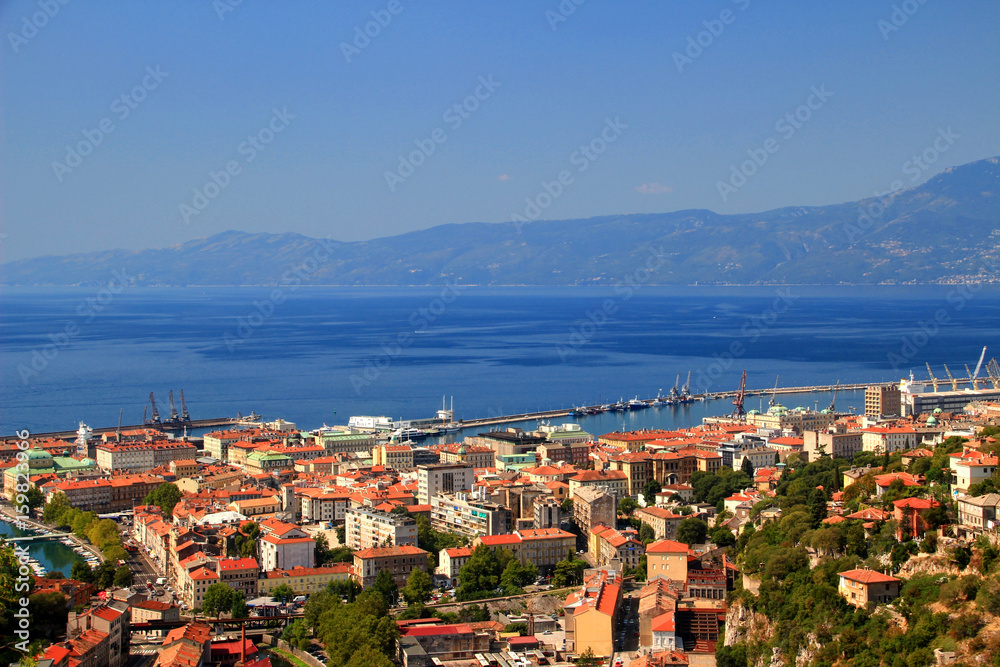 Sunny cityscape of Rijeka, the largest port of Croatia, with red rooftops of city center and the blue water of Kvarner Gulf, Adriatic Sea, in the background Ucka range, Istrian peninsula