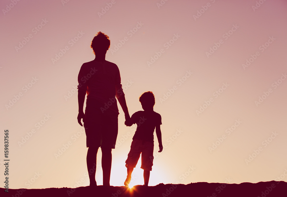 father and son silhouettes walk at sunset