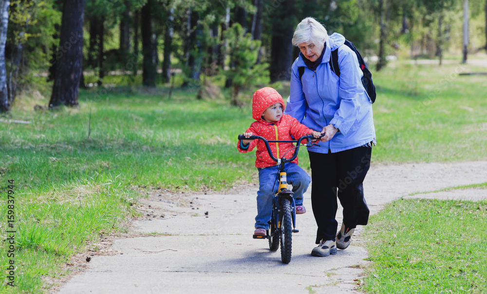 Fototapeta premium Grandmother teaching little granddaughter to ride bike