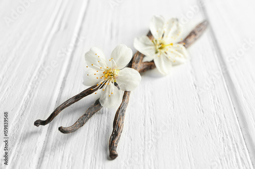Dried vanilla sticks and flowers on light wooden background, closeup