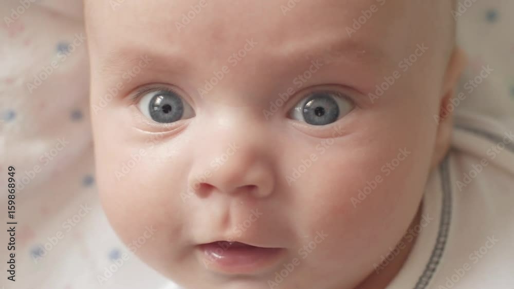The look of the baby in the camera close up shot. A cute little baby is looking into the camera. The baby looks around and then smiles and laughs. Concept of caring for children, parental love and The look of the baby in the camera close up shot. A cute little baby is looking into the camera. The baby looks around and then smiles and laughs. Concept of caring for children, parental love and