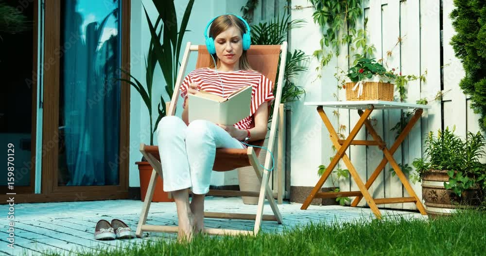 Young woman relaxing on the beach chair. Young adult reading the book and looking and smiling at camera Young woman relaxing on the beach chair. Young adult reading the book and looking and smiling at camera