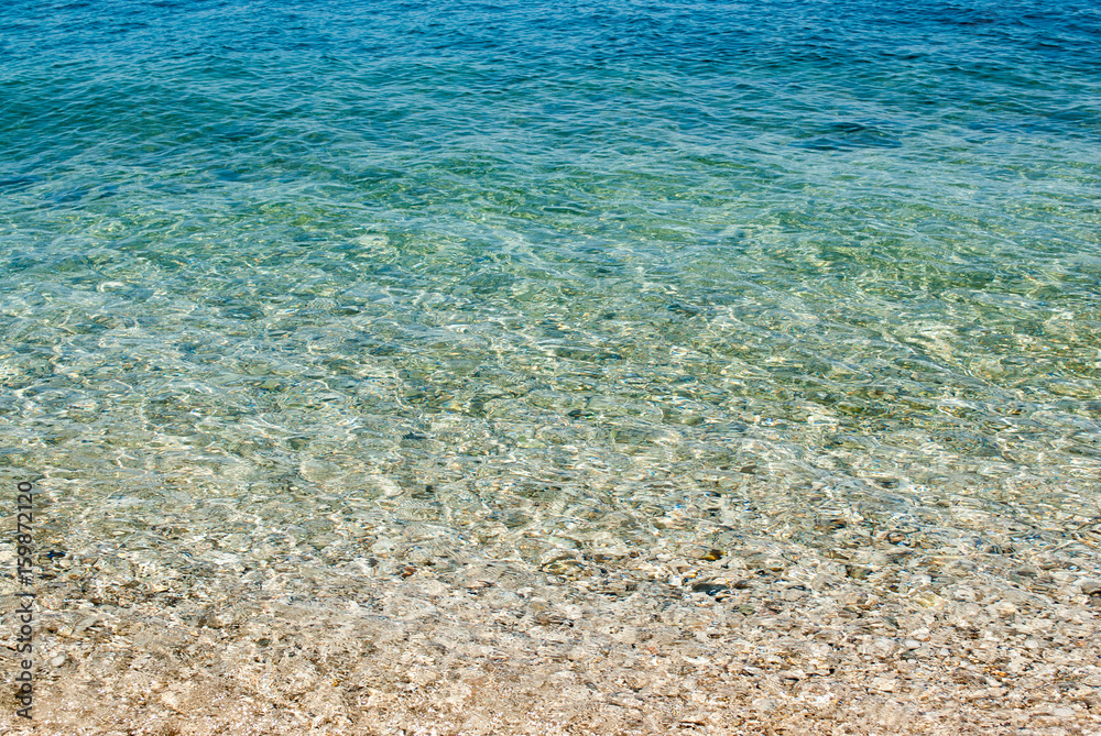 square background image of calm turquoise sea on shingle beach
