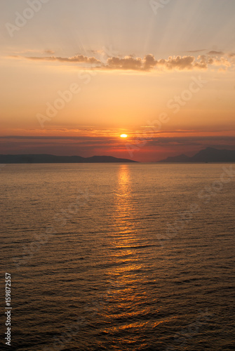 panoramic image of golden sunset with sun low above the sea and sunrays coming through clouds above 