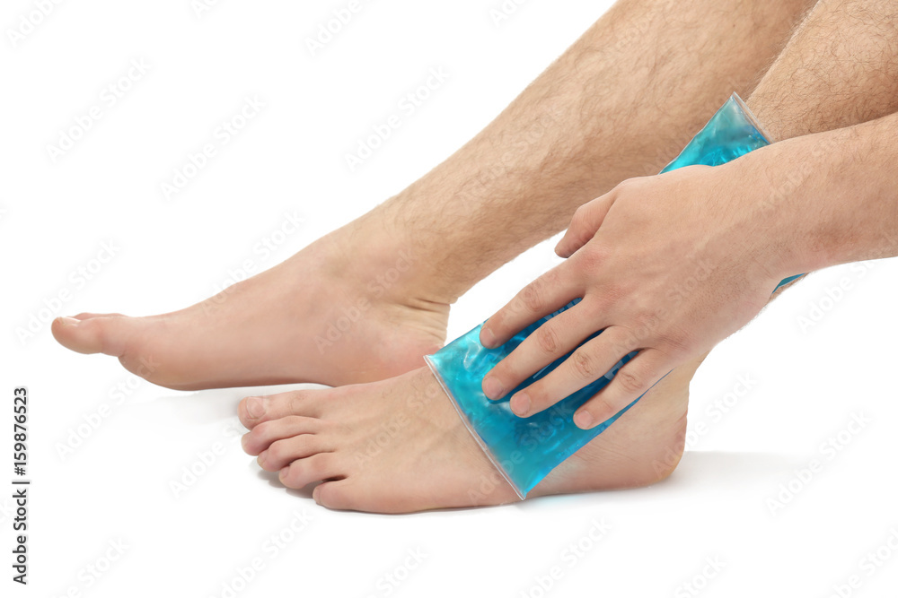 Young man applying cold compress to leg on white background, closeup