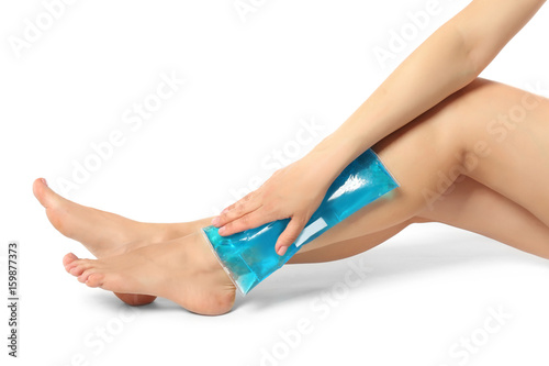 Young woman applying cold compress to leg on white background. Legs pain concept photo