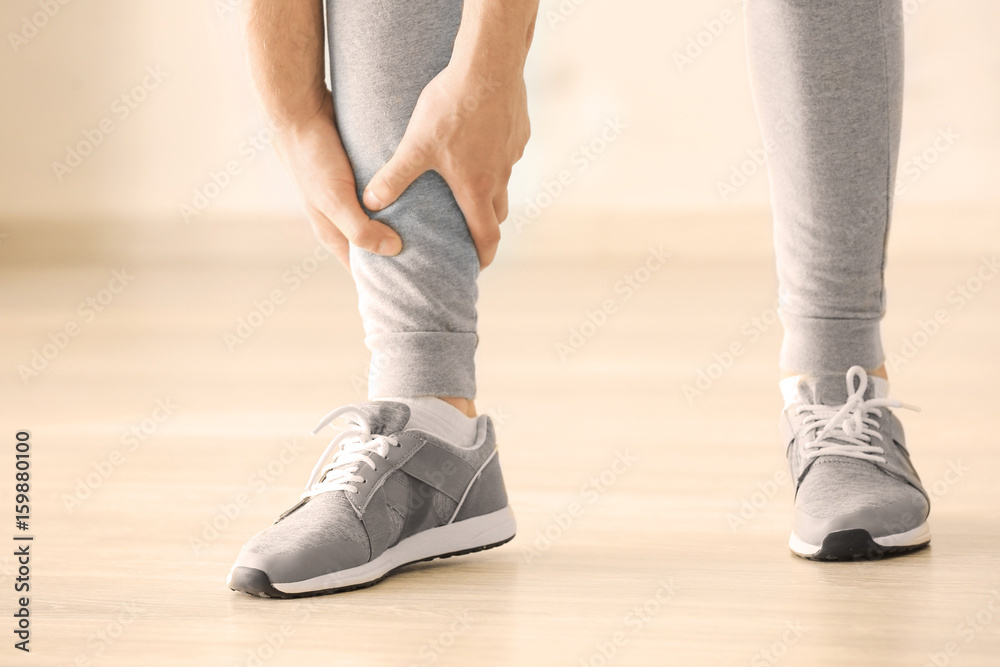 Young man suffering from pain in leg indoors Young man suffering from pain in leg indoors